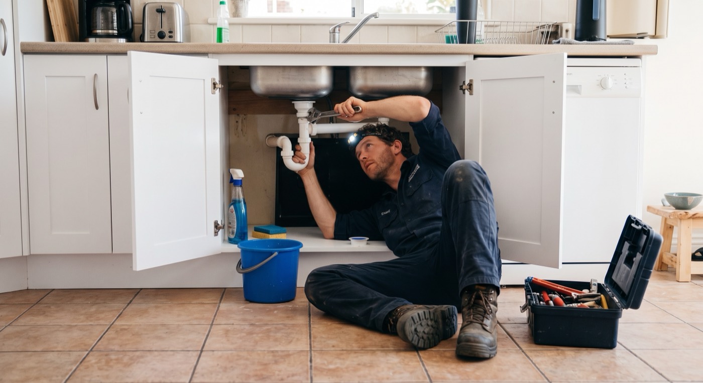Plumber repairing pipes under a kitchen sink